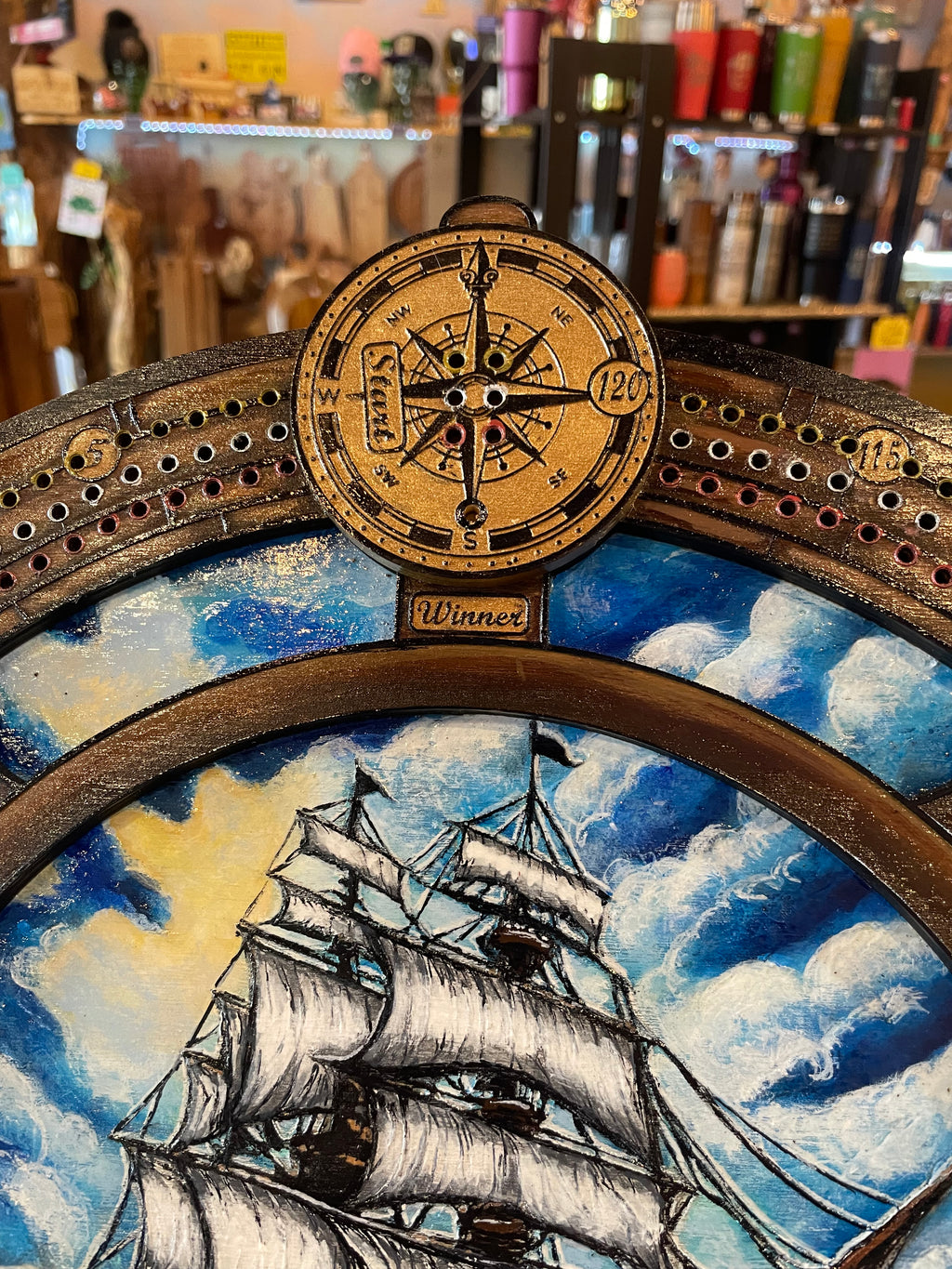 Decorative compass and ships wheel with ship illustration on a cribbage board