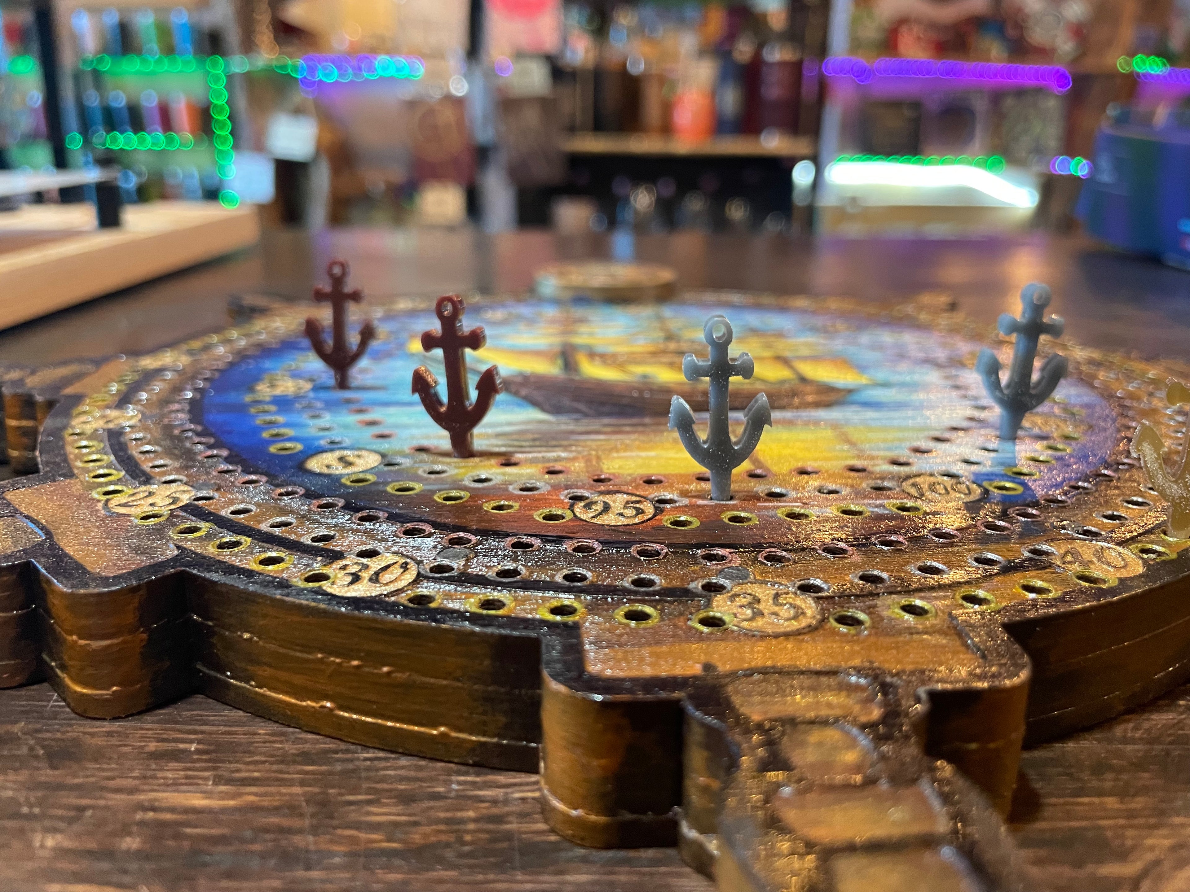 Decorative compass and ship wheel cribbage board with sunken ship and acrylic pegs.