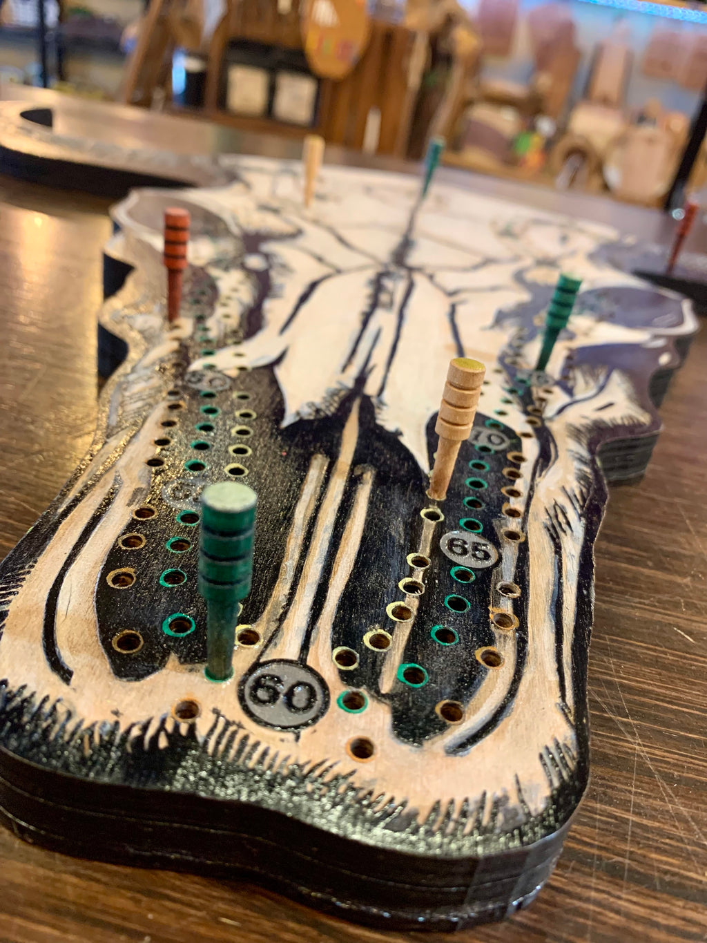 Decorative cow skull with artistic designs on a wooded cribbage board. With wooden pegs.