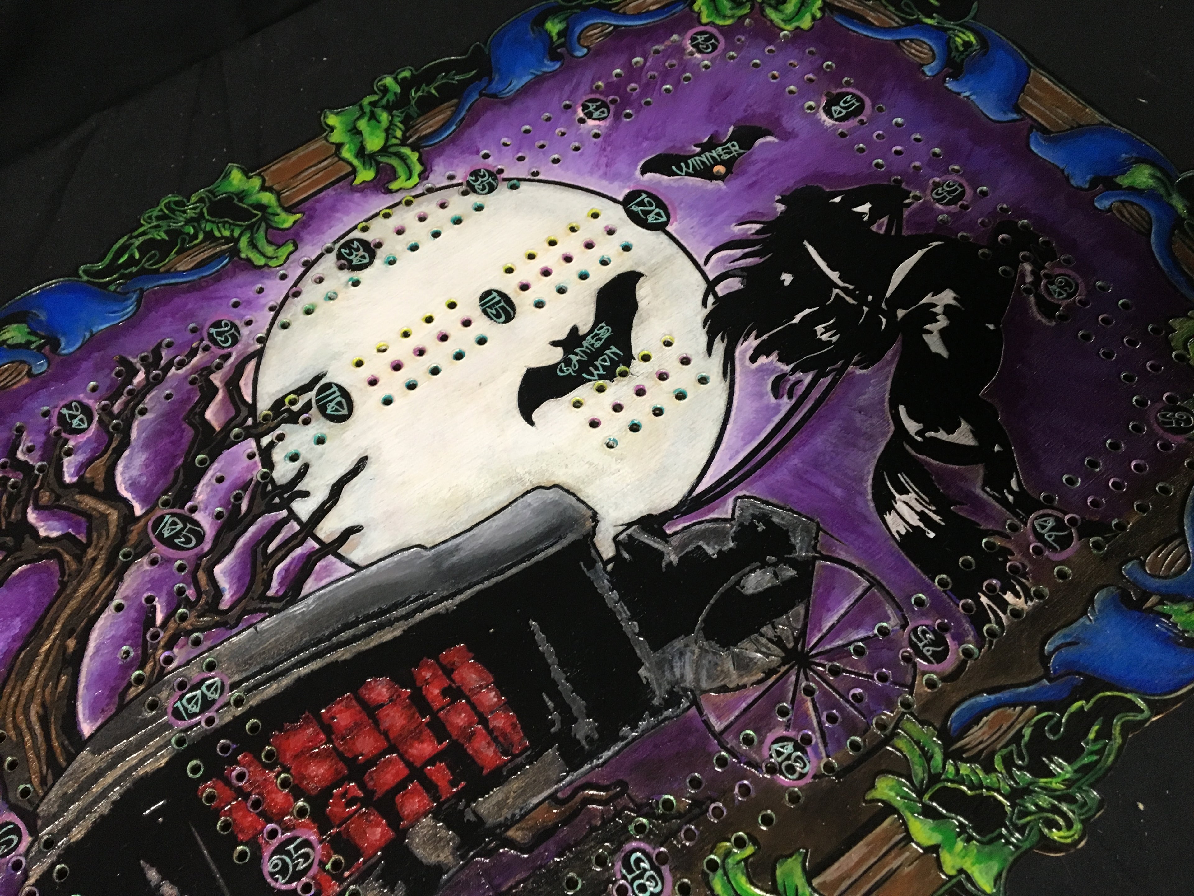 Halloween-themed cribbage board with a carriage, moon, and bats on a purple background.